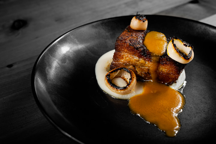 Pork belly and sauce on a black plate