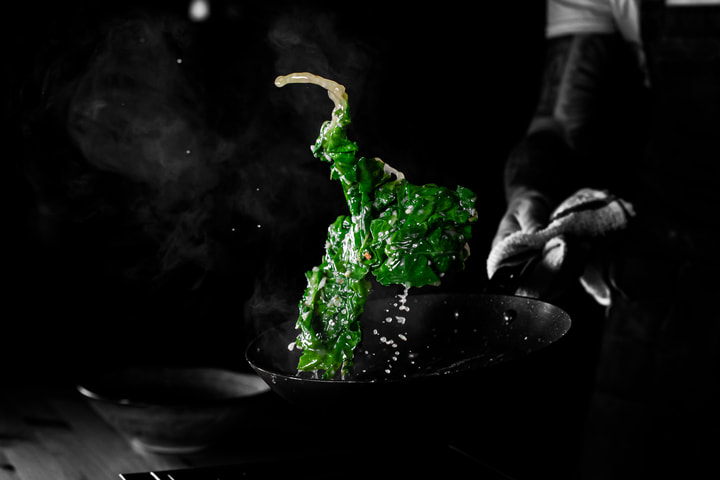 Greens tossed in the air above a pan