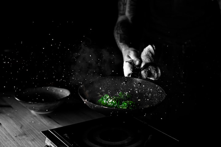 Chef seasoning greens over a stovetop